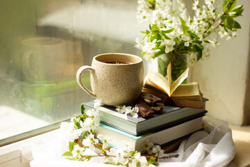 Composition of books, a cup of coffee and apricot branches on the windowsill. Morning still life