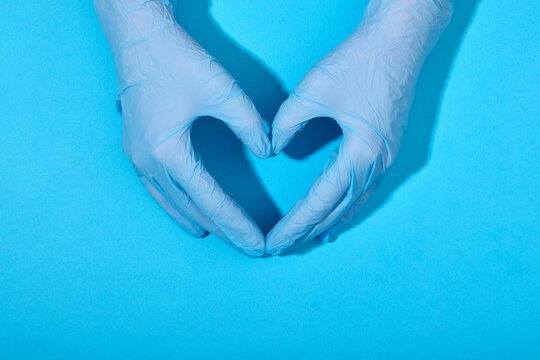Hands in latex rubber gloves lie in the shape of a heart sign on a blue background with clear shadows