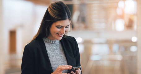 She loves getting positive feedback from her team. Cropped shot of a an attractive young businesswoman smiling while using smartphone in a modern workplace.