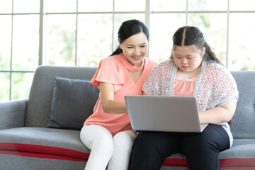 mother using laptop computer and a girl with down syndrome or her daughter, smiling and enjoying on sofa