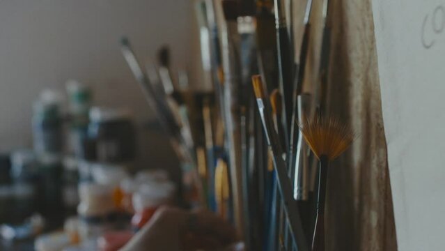 Artist choosing between a lot of painting equipment. Paint brushes macro shot with paint cans out of focus. 