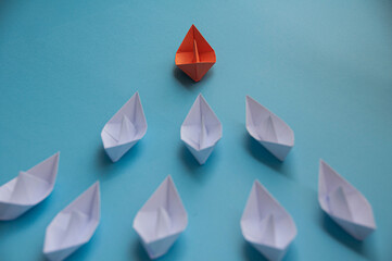 Leadership Concept - Orange color paper ship origami leading the rest of the white paper ship on blue cover background. Copy space concept