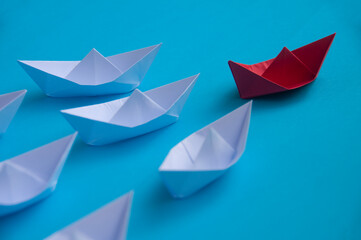 Leadership Concept - Red color paper ship origami leading the rest of the white paper ship on blue...