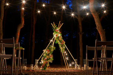 Festive string lights illumination on boho tipi arch decor on outdoor wedding ceremony venue in...