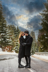 couple kissing against the backdrop of a snow-covered mountain forest and a highway