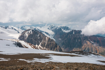 Dramatic landscape with large glacier and high snow mountains in cloudy sky. Wonderful view from stone hill with snow to glacier and snowy mountain peak and low clouds. Top view to majestic mountains.