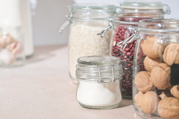 glass jars with grains, nuts and sugar on a kitchen table. sustainable home grocery storage and zero plastic house. eco friendly kitchen.