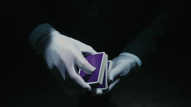 Close-up of a Suited Magician's Hands Performing Sleight of Hand Card Tricks. Plain cover of a deck of cards. Cards fly and turn over in the air. Slow Motion. Background is Black.