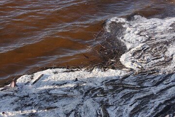 Foam and debris near the shore during a spill on the river