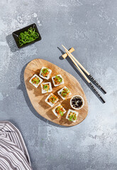 Maki roll with fried carrot and green onion top on wooden board in contemporary composition. Sushi roll with chopsticks on concrete table. Maki sushi in minimal style.