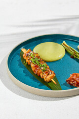 Squid yakitori in ceramic dish on white background. Japanese skewered squid with wasabi sauce. Grilled kalmar on bamboo skewer in asian style. Food menu for izakaya. Summer pan asian menu. © Ryzhkov