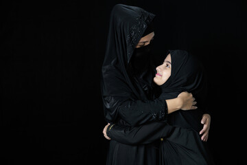 muslim woman and her daughter smiling and hugging together on black background