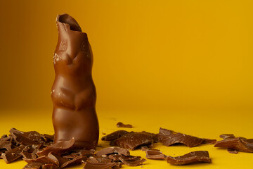 Chocolate Easter bunny with bitten ears and pieces scattered around. Copy space on yellow...