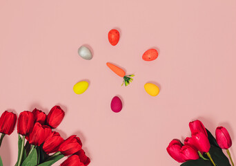 Easter eggs, carrot and red tulips on pastel pink background. Horizontal flat lay composition, minimal easter and spring celebration concept
