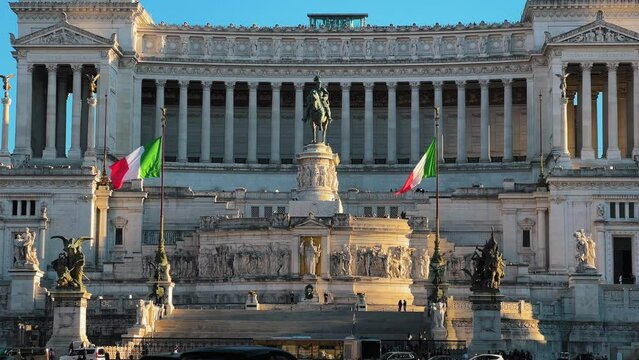 SLow motion wide shot of waving italian flags and Altar of Fatherland building in background - In foreground walking tourist in Rome