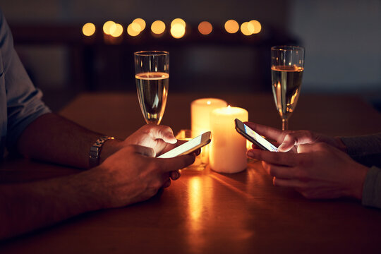 Lets Let Everyone Know Were Engaged. Cropped Shot Of A Unrecognizable Couple Texting On Their Mobile Phones Over A Candle Lit Dinner At Night.