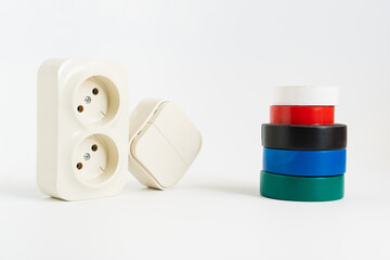 multicolored insulating tape, double socket and two-key light switch on white background. mechanical device for switching lighting circuit, two sockets connected by monolithic case. electronic devices