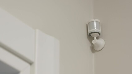 Smart home wireless motion sensor for alarm system and smart home automation, small plastic white motion detector installed in the living room. High quality 4k footage