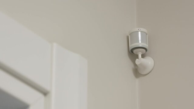 Smart home wireless motion sensor for alarm system and smart home automation, small plastic white motion detector installed in the living room. High quality 4k footage