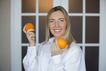 Portrait of a young smiling girl in a white shirt with oranges in her hands