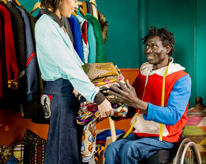 two tailors in their shop workshop passing fabrics to create clothes, example of small business and...
