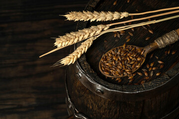 Barley malt for dark beer on a barrel in a bowl with a spoon, dark background. Ingredient for beer.