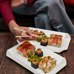Bright sushi on a background of wooden table, female hand holding a roll.