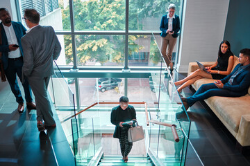 Lets get this day started. Shot of a young businesswoman walking up the stairs while using a digital tablet in a busy office at work.