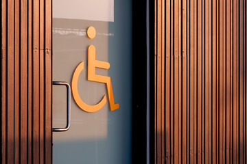 Perspective side view of disabled wheelchair restroom sign on glass sliding door with wooden wall...