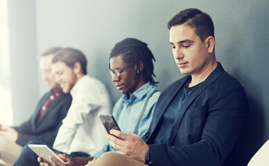 Getting some advice and tips online for the interview. Shot of a group of businessmen using different wireless devices while waiting in line for an interview.