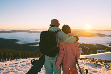 Snowboarders couple enjoying sunset in ski resort beautiful mountains