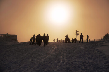 Fototapeta na wymiar Silhouettes of resting snowboarders and skiers in the ski resort at sunset on the top of the mountain