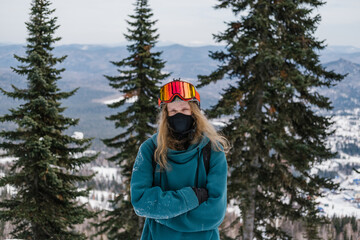 Fototapeta na wymiar Portrait of snowboarder man wearing long hair standing in the forest on the slope of a ski resort