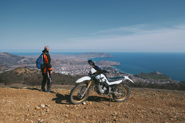 Active elderly man riding enduro motocross motorcycle pit bike in beautiful mountains hills and sea landscape