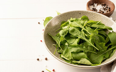 Fresh arugula leaves in white bowl with spices