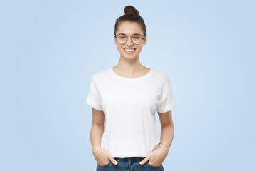 Young attractive european woman stands with hands in pockets, wearing blank white t-shirt