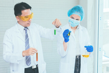 Scientist team in uniform holding beaker and test tube have chemical liquid for testing chemical reaction.