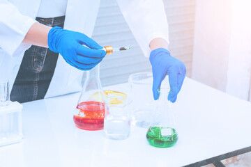 Hand of Scientist in uniform holding beaker and test tube have chemical liquid for testing chemical reaction.