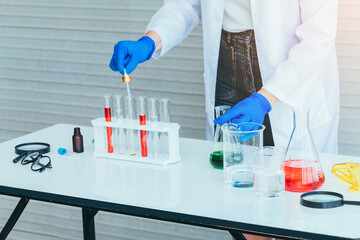 Hand of Scientist in uniform holding beaker and test tube have chemical liquid for testing chemical reaction.