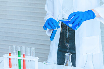 Hand of Scientist in uniform holding beaker and test tube have chemical liquid for testing chemical reaction.