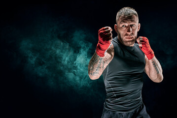 Kickboxer in red bandages is boxing against a background of smoke. The concept of mixed martial...
