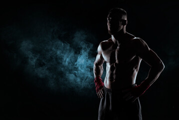 Kickboxer in red bandages poses against a background of smoke. The concept of mixed martial arts.