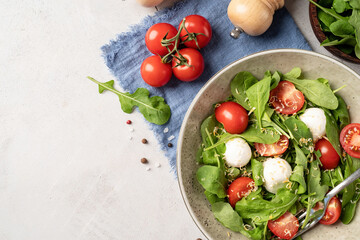 Fresh salad with arugula, cherry tomatoes, mozzarella cheese and hard cheese on white wooden background. Top view