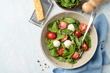 Fresh salad with arugula, cherry tomatoes, mozzarella cheese and hard cheese on white wooden background. Top view