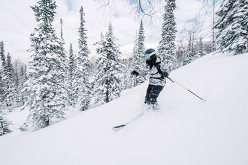Fototapeta na wymiar Skier female moving in snow powder in forest on a steep slope of ski resort. Freeride, winter sports outdoor