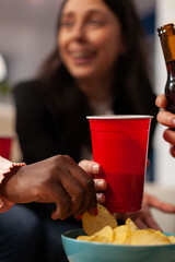 Cheerful people enjoying office party celebration with drinks and snacks after work hours. Coworkers eating chips from bowl, holding glasses and bottles of beer, doing fun activity. Close up.