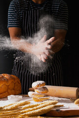 Hand of a man clapping and sprinkling white flour over over donut on wooden table in his house.
