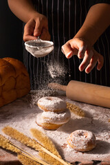 Hand of a man sprinkling white flour over over donut on wooden table in his house.