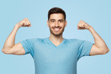 Strong and sporty athletic man in casual blue t-shirt, showing two biceps after training in gym - obrazy, fototapety, plakaty