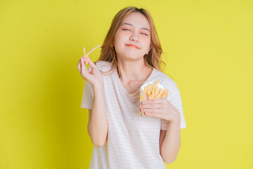 Image of young Asian girl eating french fries on yellow background